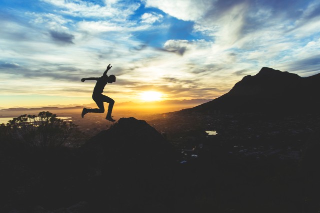 Man jumping in the evening with city below a hill in the background. It's almost dark and very atmospheric.