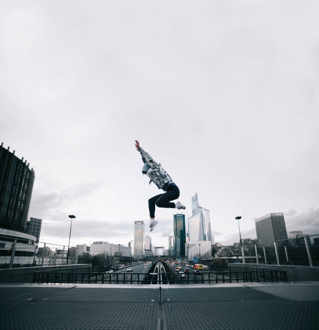 Woman jumping high on a bridge - the Paris skyline in the back. It's a bit gray that day.